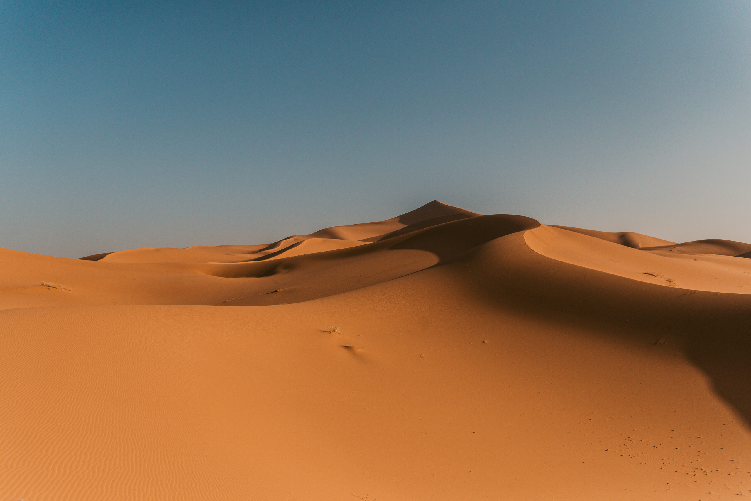 geschwungene Wüstenlandschaft mit orangem Sand im sanften Abendlicht von Marokko - offlinepleasure.at