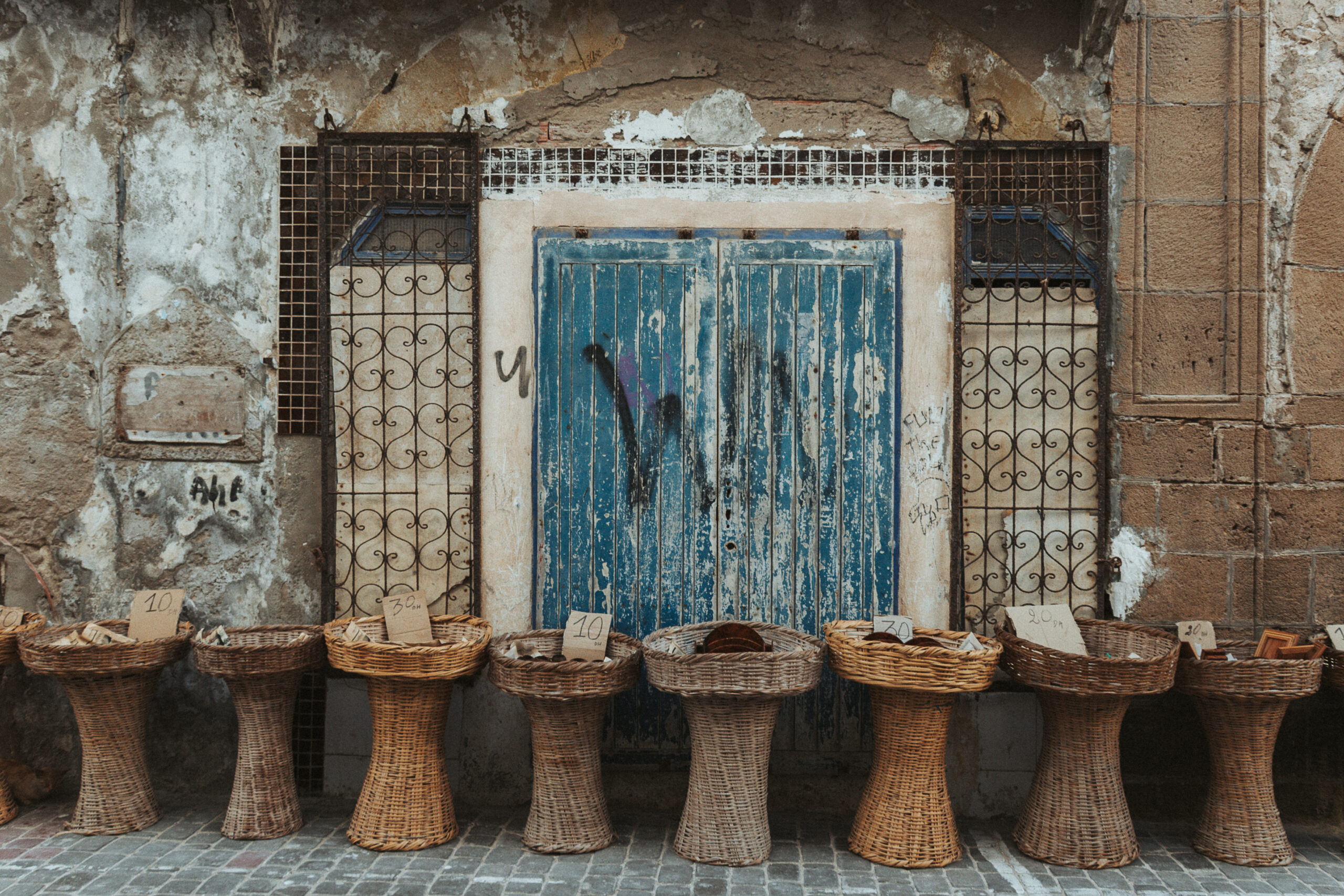 Hausmauer mit blauem Tor und Verkaufskörbe in Marokko - offlinepleasure.at